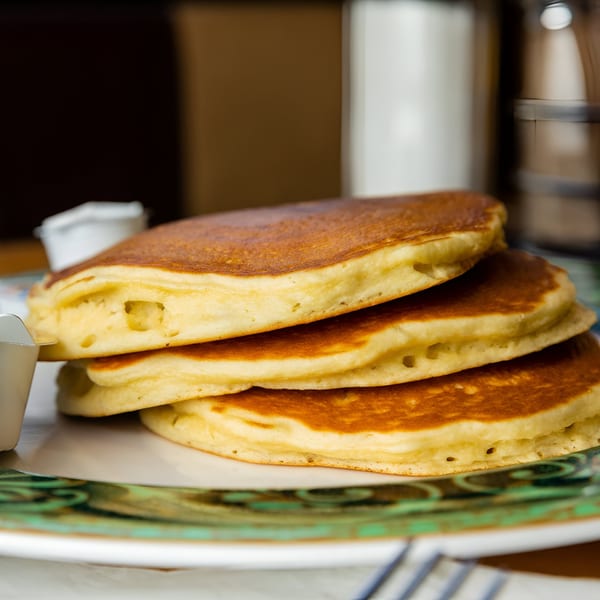 Stack of three golden-brown pancakes on a decorative green and white plate at Georgia Diner.