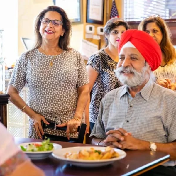 Smiling people, including a man in a red turban, enjoying a meal at Georgia Diner.