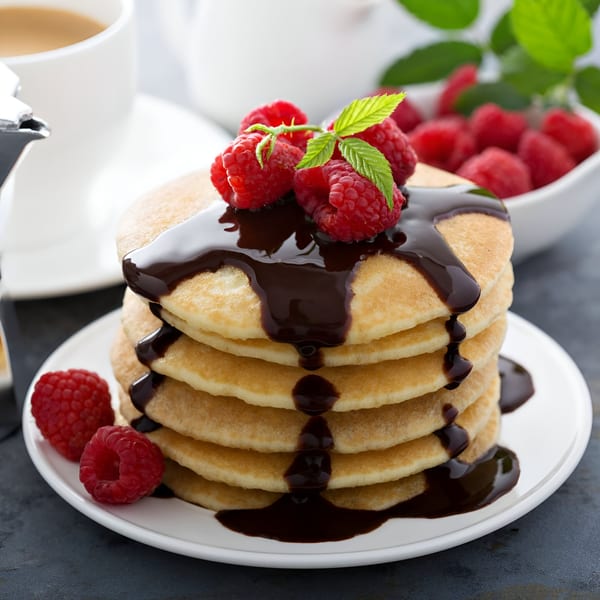 Stack of Georgia Diner pancakes with chocolate syrup, fresh raspberries, and mint, with coffee.