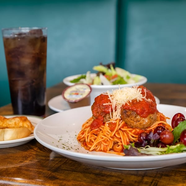 Spaghetti and meatballs with a side salad, garlic bread, and a soda on a wooden table.