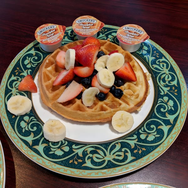 A Georgia Diner waffle topped with strawberries, blueberries, and bananas, with three syrup cups.