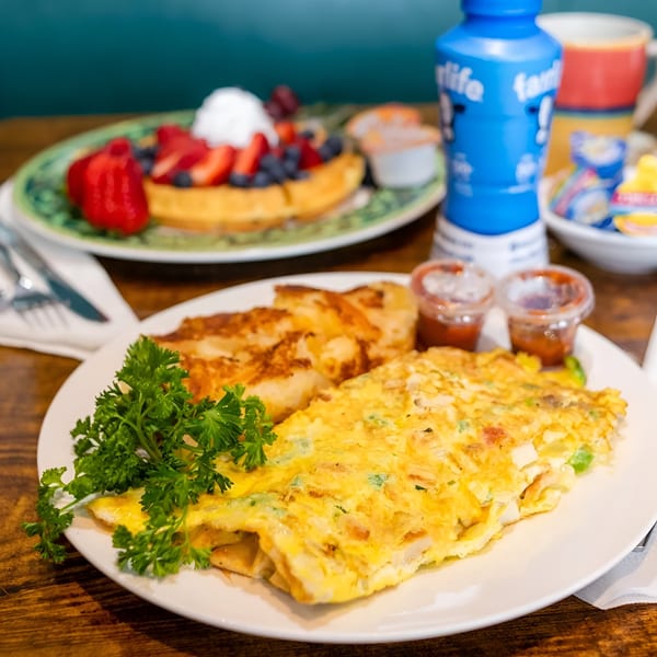 A Georgia Diner omelet with hash browns and parsley, with a fruit waffle in the background.